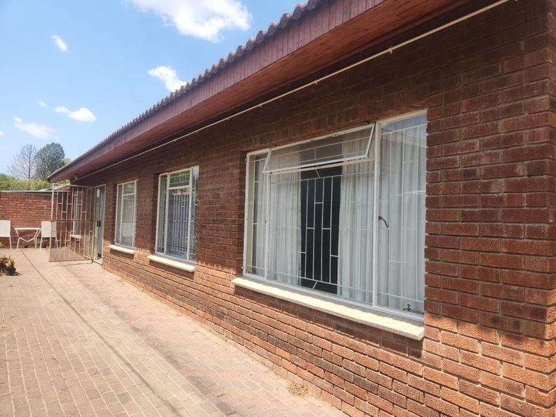 Rear exterior view of the townhouse featuring a face brick facade, tiled roof, and paved walkway with security bars on windows.