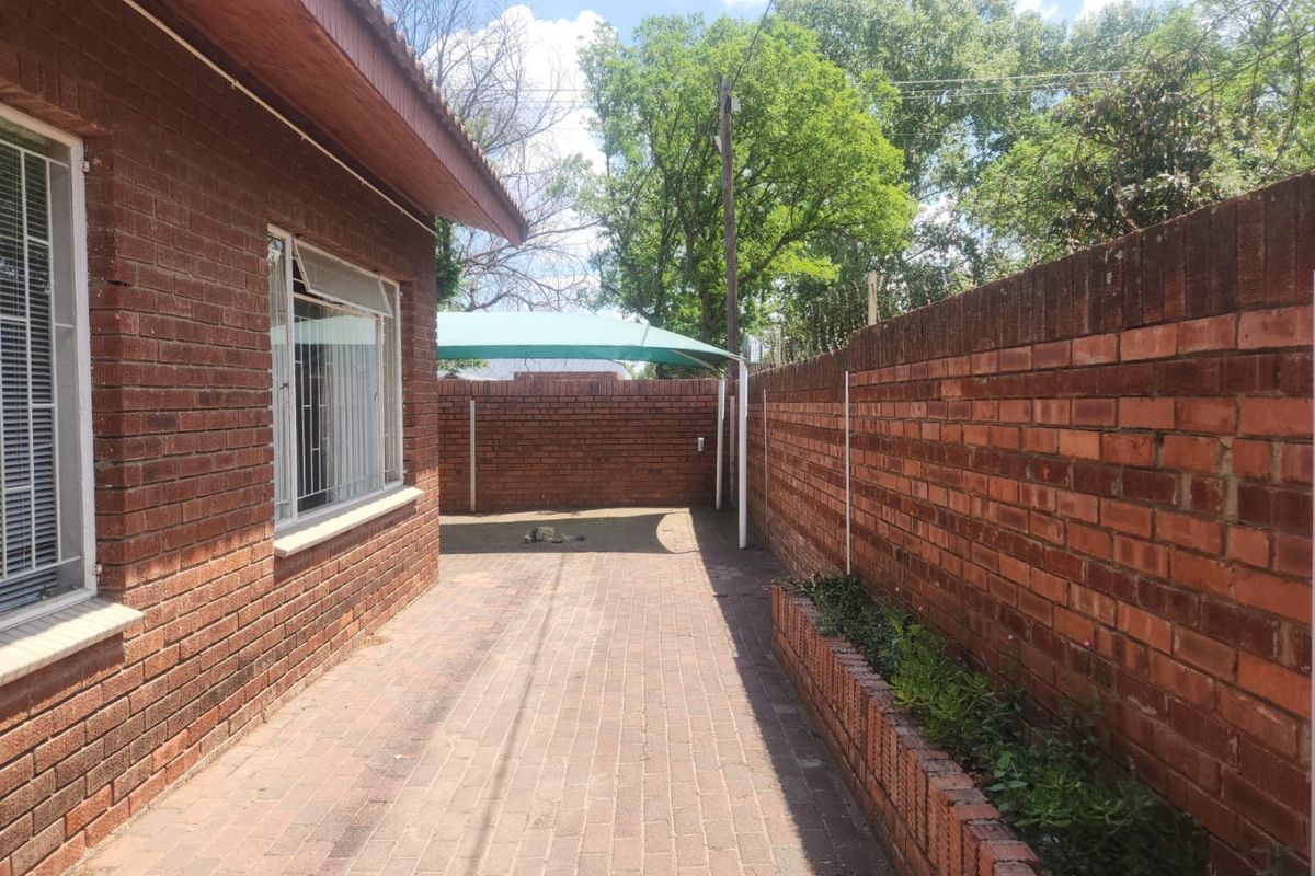 A private rear courtyard featuring face brick walls, paved flooring, a built-in brick planter, and a shade sail structure.