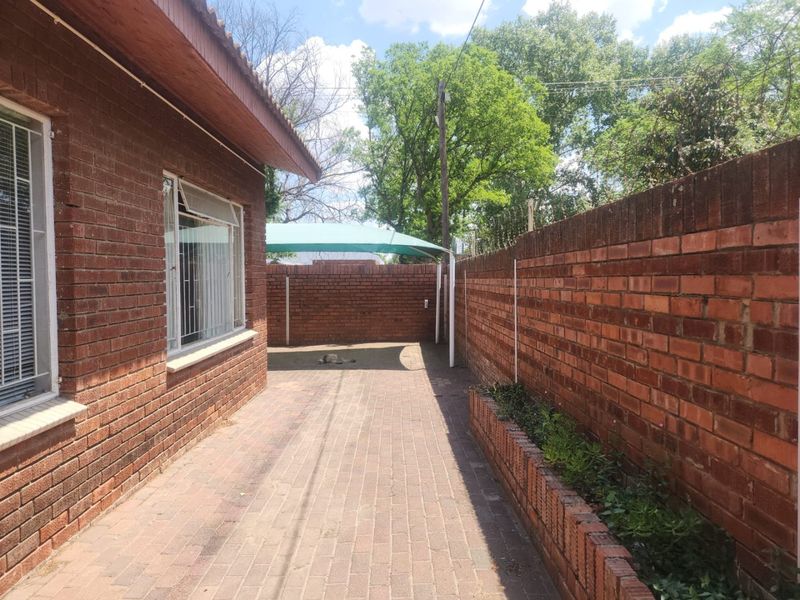 A private rear courtyard featuring face brick walls, paved flooring, a built-in brick planter, and a shade sail structure.