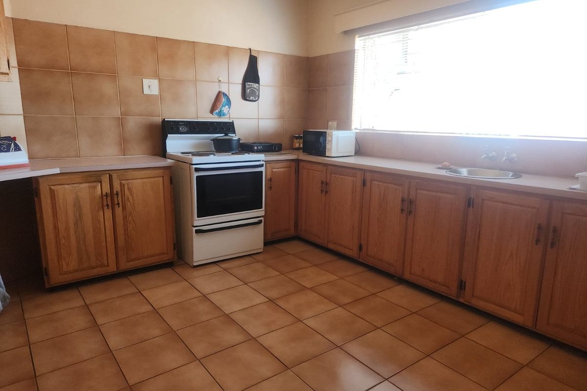 A functional kitchen featuring wooden cabinetry, tiled backsplash, tiled flooring, and a freestanding stove with ample counter space.