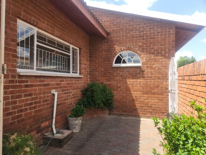A rear exterior view of the townhouse featuring a paved patio area, classic brick facade, and an arched window detail.