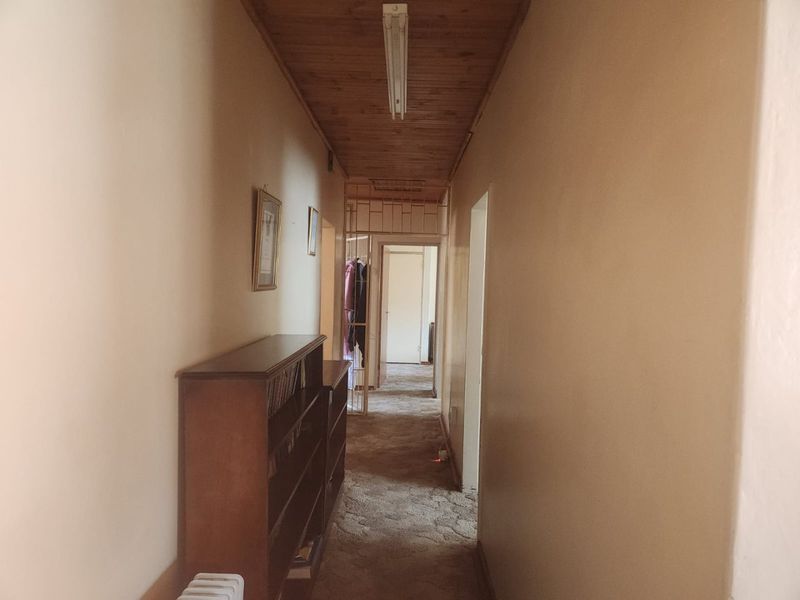 A long residential hallway featuring a timber-clad ceiling, fluorescent lighting, and a security gate leading to further rooms.