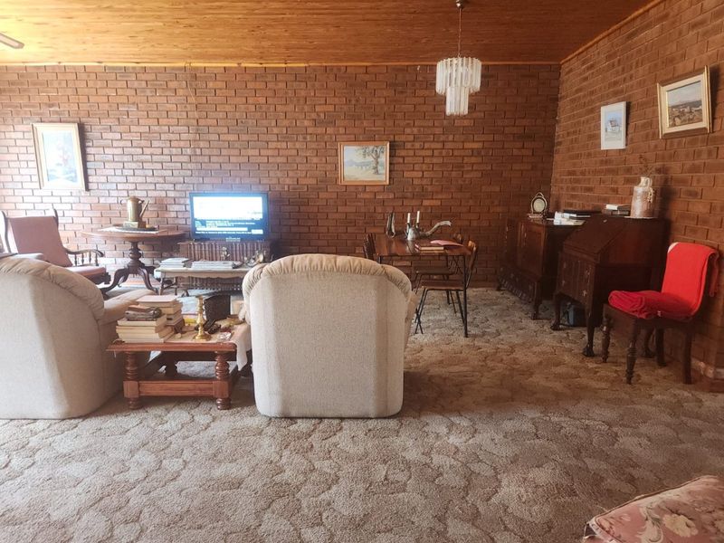 Spacious living area featuring classic exposed brick walls, a warm timber ceiling, and carpeted flooring, offering a traditional aesthetic with potential for modern updates.