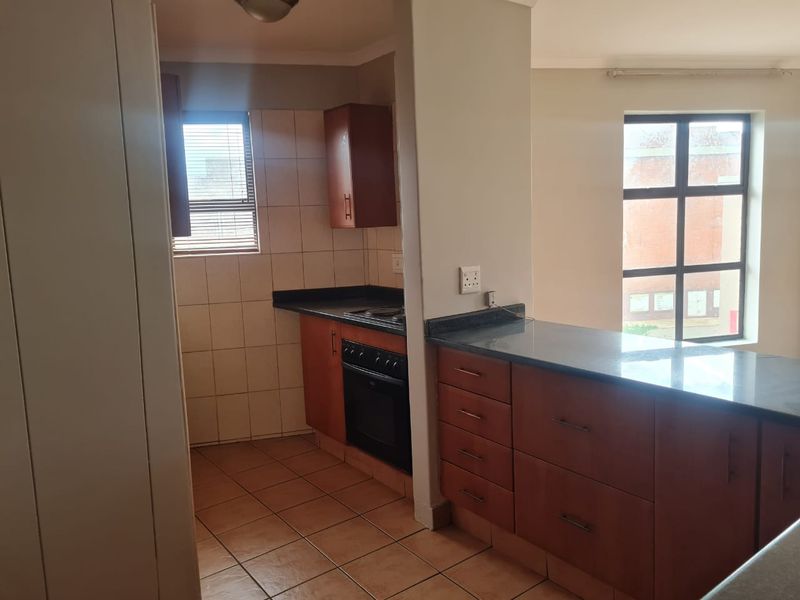 A functional kitchen featuring wooden cabinetry, granite countertops, built-in oven and hob, with tiled flooring and backsplash.