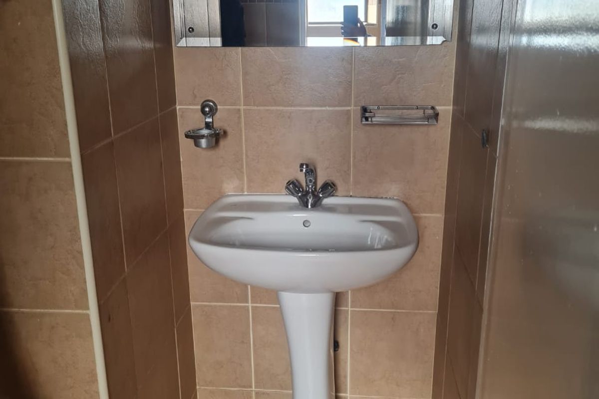 A compact bathroom featuring a white pedestal basin, chrome fixtures, and neutral ceramic wall and floor tiling.