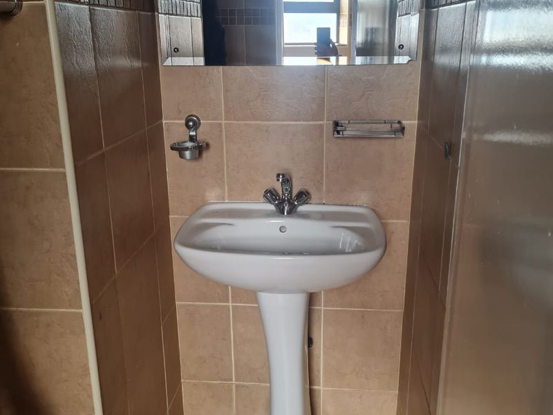 A compact bathroom featuring a white pedestal basin, chrome fixtures, and neutral ceramic wall and floor tiling.