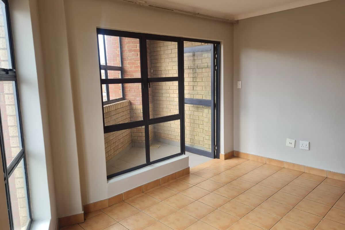 An empty living area featuring tiled flooring and large aluminium-framed windows and doors leading to an enclosed balcony space.
