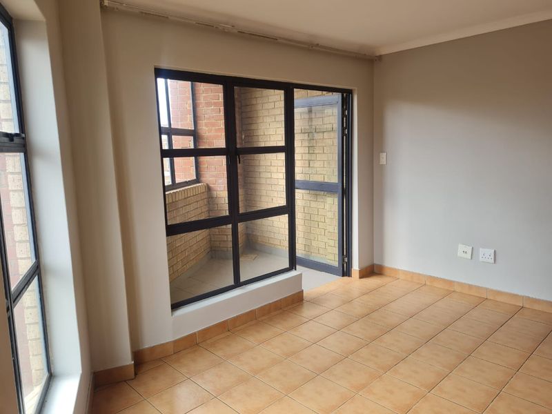 An empty living area featuring tiled flooring and large aluminium-framed windows and doors leading to an enclosed balcony space.