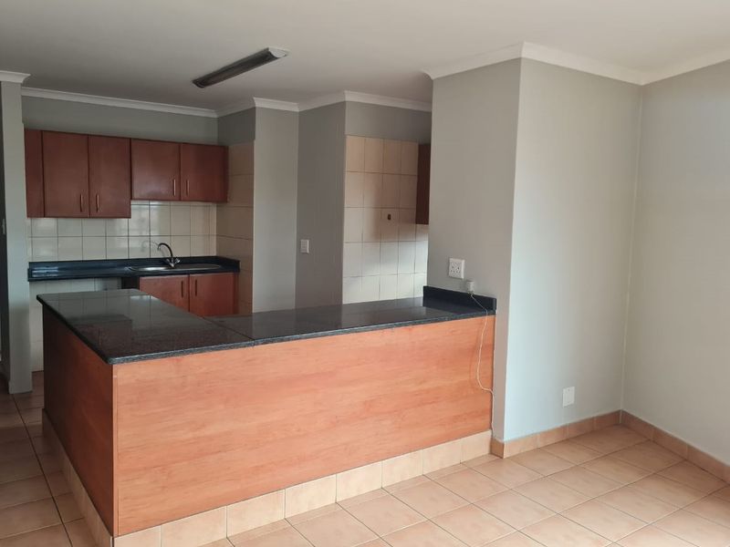 Open plan kitchen featuring granite countertops, laminate cabinetry, and a breakfast bar, seamlessly flowing into the living area with tiled flooring.