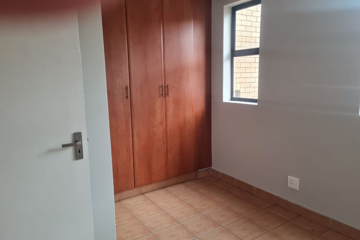 A compact, empty bedroom featuring tiled flooring, a built-in wooden wardrobe, and a window providing natural light.