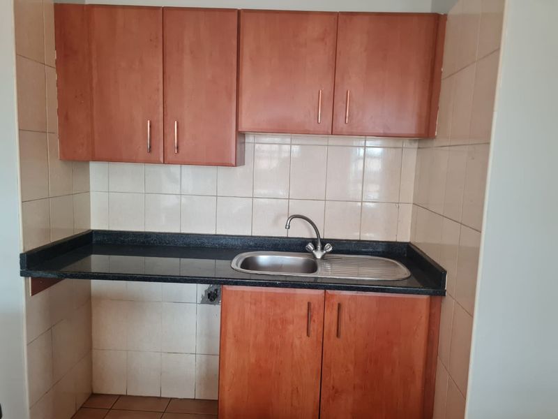 A compact kitchen featuring wooden cabinetry, a granite countertop, and a stainless steel sink with tiled splashbacks.