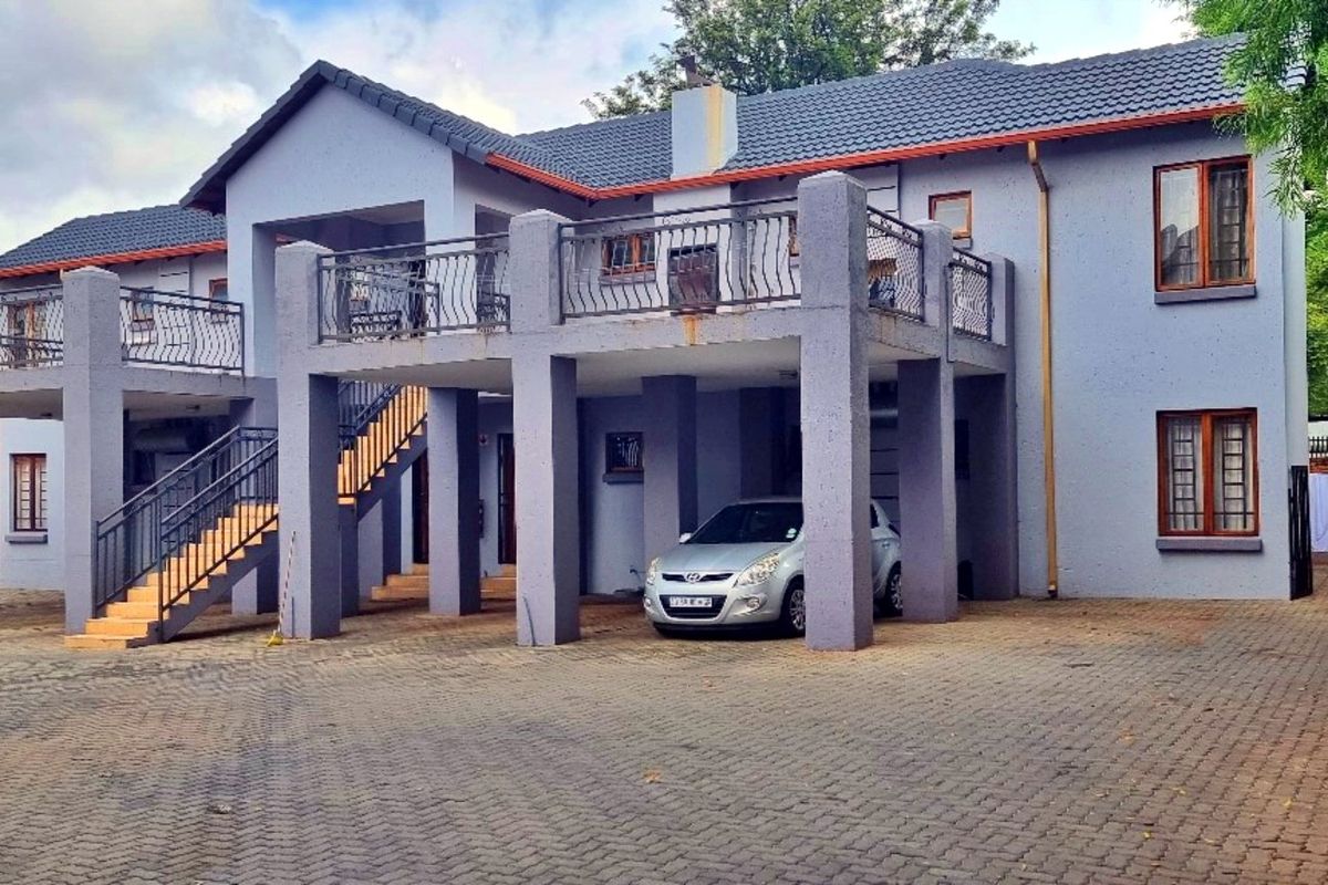 Front elevation of a multi-story townhouse featuring a paved driveway, elevated balconies with wrought iron railings, and an external staircase.