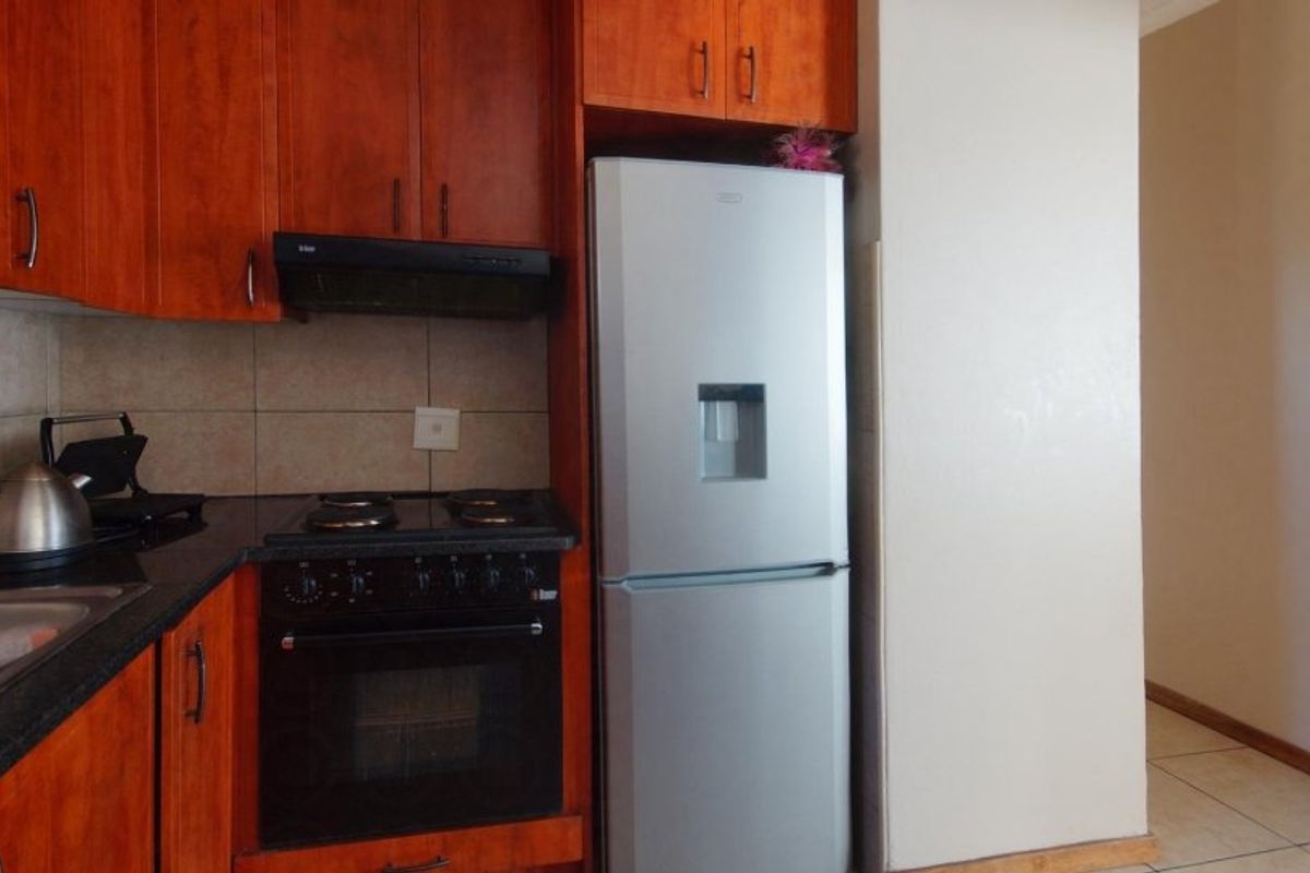 A functional kitchen featuring warm-toned wooden cabinetry, dark countertops, a built-in oven with hob, and tiled flooring.