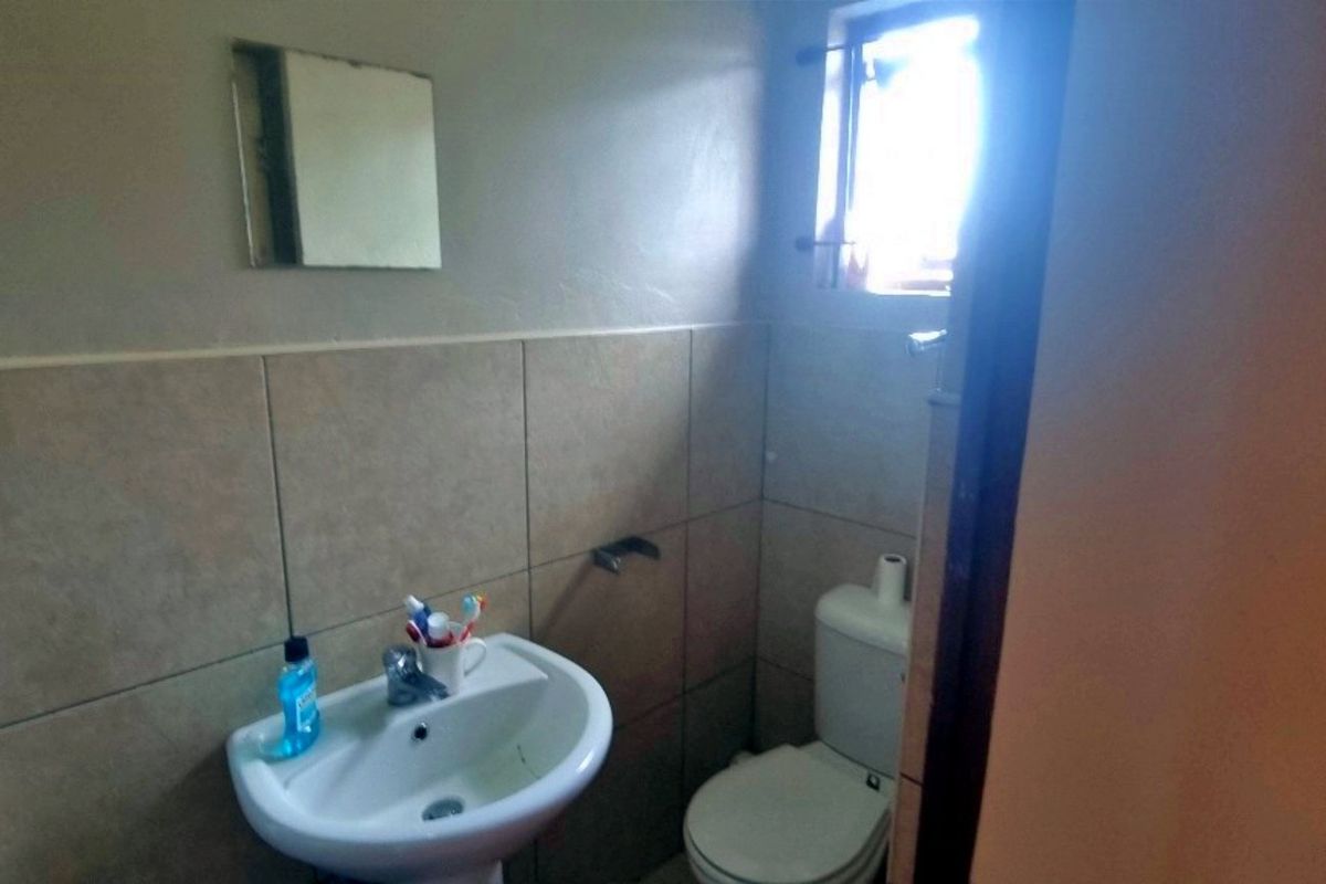 A functional bathroom featuring a pedestal basin, toilet, and neutral wall tiling with natural light from a small window.