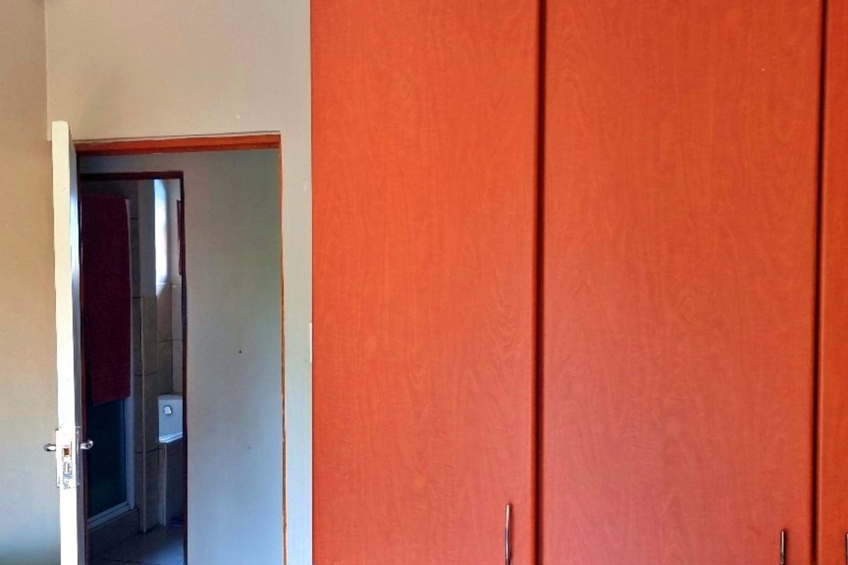 A bedroom interior featuring built-in wooden cupboards and a doorway leading to an adjacent bathroom area.