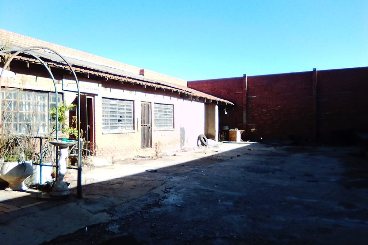 Rear exterior view of a commercial property featuring a concrete yard, brick boundary walls, and a building structure with security gates and louvre windows.