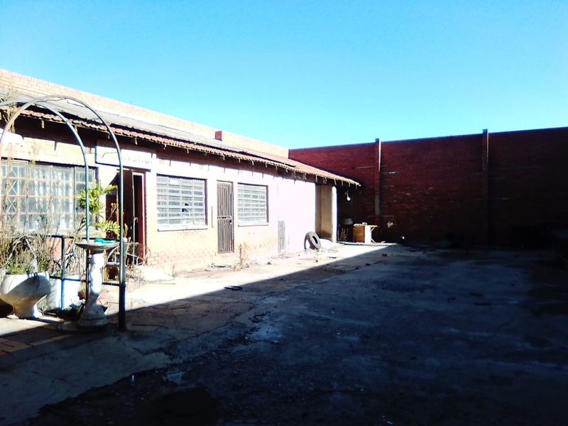 Rear exterior view of a commercial property featuring a concrete yard, brick boundary walls, and a building structure with security gates and louvre windows.