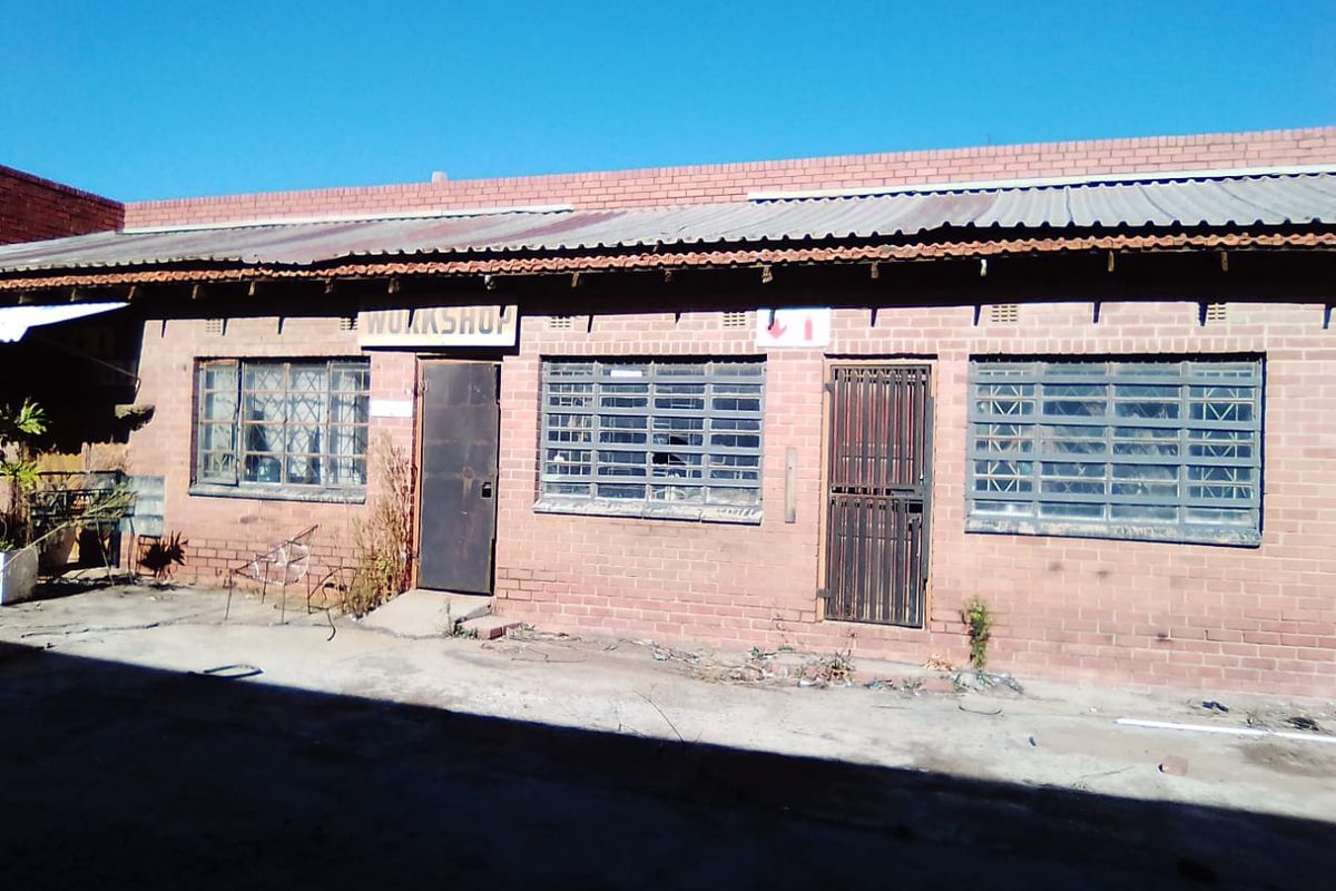 Exterior view of a commercial workshop building featuring brick construction, corrugated metal roofing, and security-fitted windows and doors.