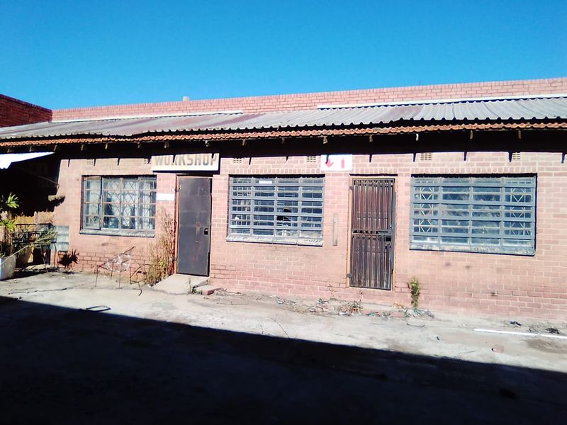 Exterior view of a commercial workshop building featuring brick construction, corrugated metal roofing, and security-fitted windows and doors.