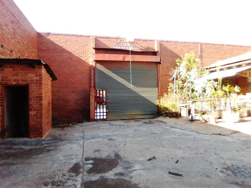 Rear exterior yard area featuring a large industrial roller shutter door, exposed brick walls, and concrete paving in a commercial setting.