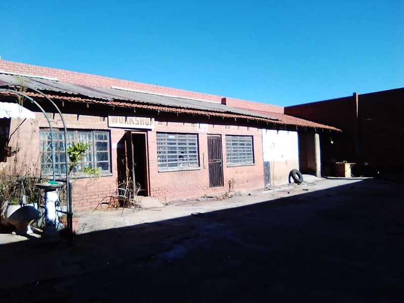 Rear exterior view of a commercial workshop building featuring brick construction, steel-framed windows, and a concrete yard area.