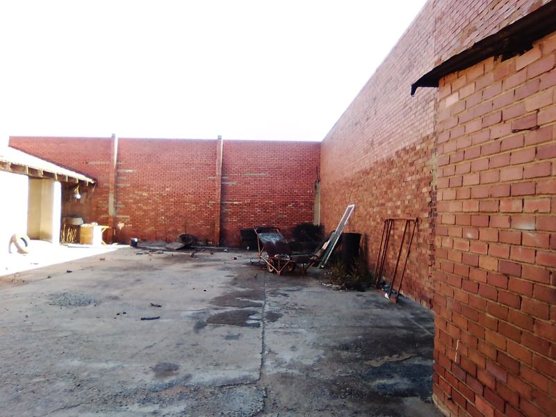 An expansive, open-air rear yard area featuring high brick boundary walls and a concrete surface, suitable for commercial storage or redevelopment.