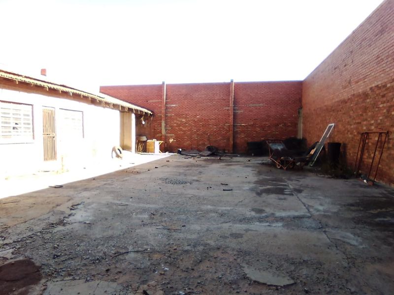 A spacious rear yard area featuring exposed brick boundary walls and a concrete surface, suitable for commercial storage or utility use.
