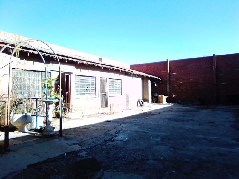 Rear exterior view of a commercial property featuring a concrete yard, brick boundary wall, and building facade with security bars and damaged window panes.