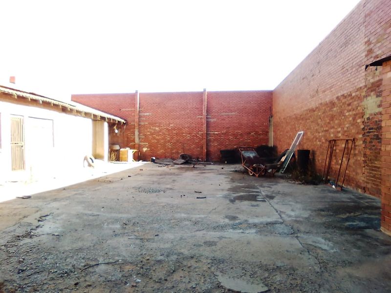 An expansive, open-air rear yard featuring exposed brick boundary walls and a weathered concrete surface, offering significant potential for redevelopment or functional commercial use.