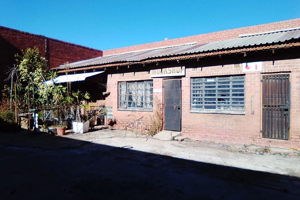 Rear exterior view of a commercial workshop building featuring brick construction, security-barred windows, and a concrete courtyard area.