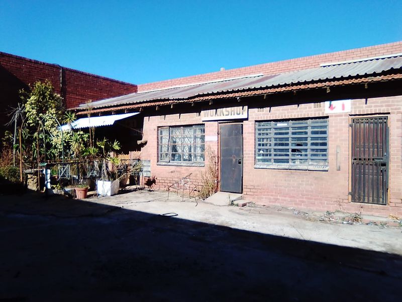 Rear exterior view of a commercial workshop building featuring brick construction, security-barred windows, and a concrete courtyard area.