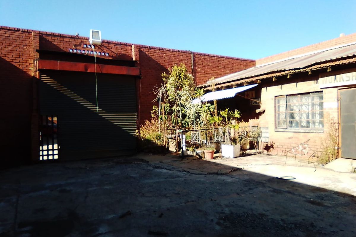 Rear exterior courtyard of a commercial property featuring a large roller shutter door, brick walls, and concrete paving in need of maintenance.