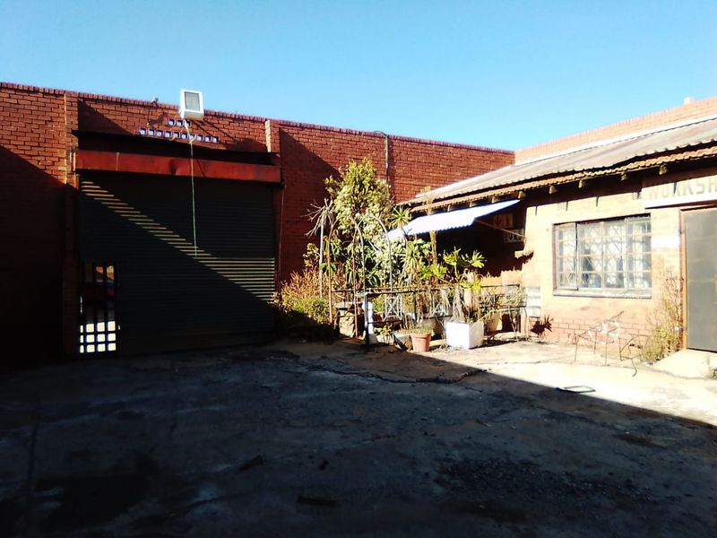 Rear exterior courtyard of a commercial property featuring a large roller shutter door, brick walls, and concrete paving in need of maintenance.