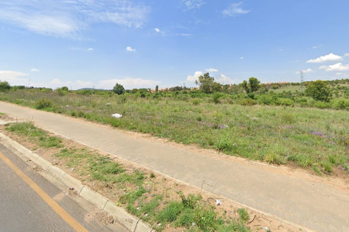 A view of the vacant residential land from the adjacent street, showing the plot's accessibility and surrounding landscape.