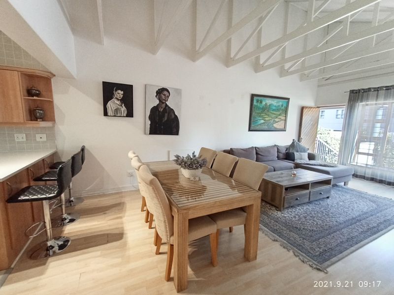 Spacious open-plan living and dining area featuring high vaulted ceilings with exposed trusses, laminate flooring, and direct access to an outdoor balcony.