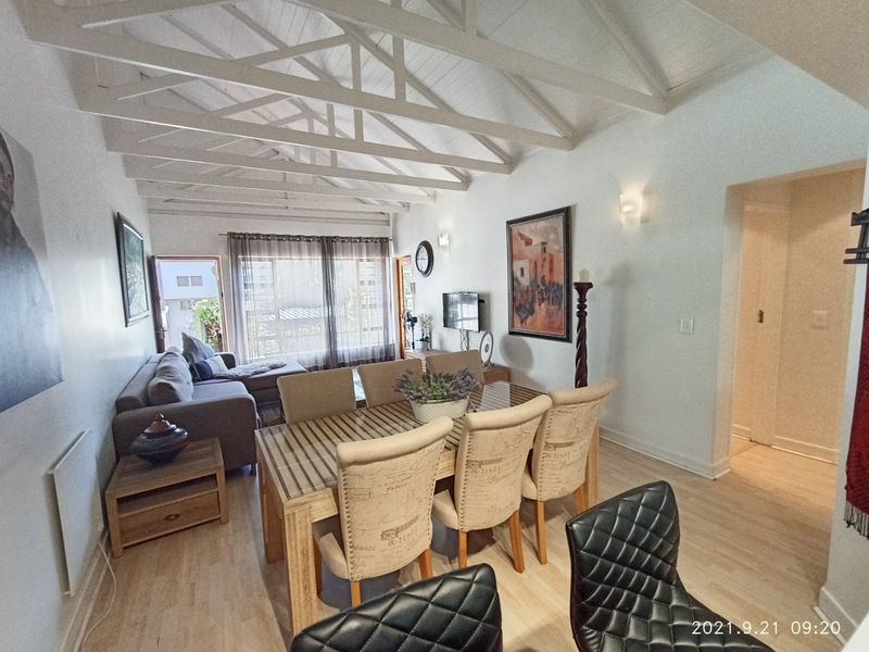 Open-plan living and dining area featuring high vaulted ceilings with exposed timber trusses and light-toned laminate flooring.