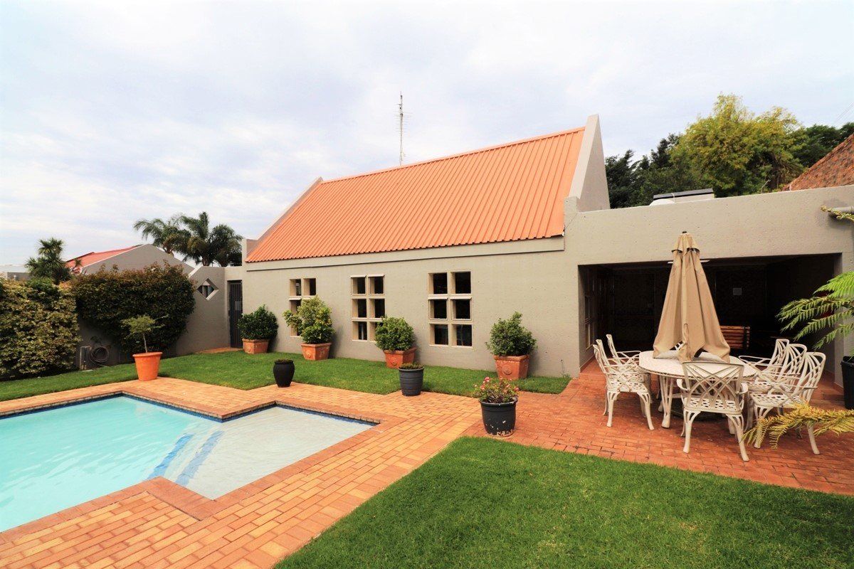Rear exterior view featuring a swimming pool, brick paved patio area, and a well-maintained lawn with a pitched metal roof structure.