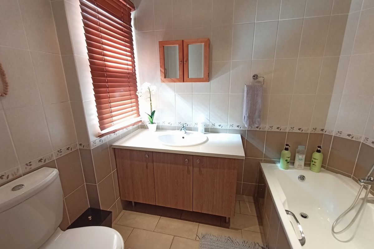 A functional bathroom featuring a vanity cabinet with integrated sink, a bathtub, a toilet, and neutral wall tiling with decorative border accents.