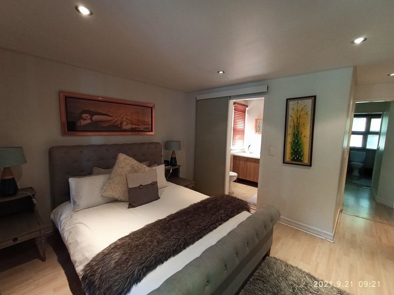 A well-maintained bedroom featuring recessed downlighting, laminate flooring, and an en-suite bathroom accessible via a sliding door.