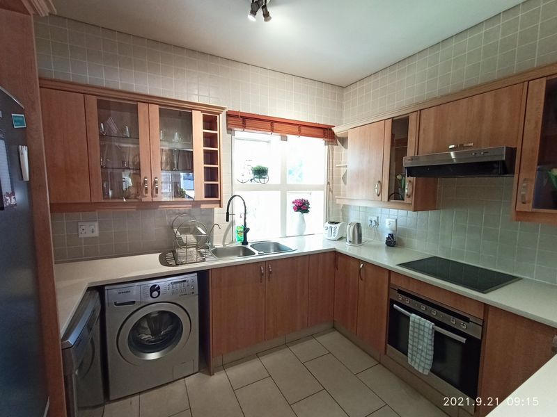 A functional kitchen featuring wood-finish cabinetry, laminate countertops, a built-in oven with hob, and tiled finishes throughout.