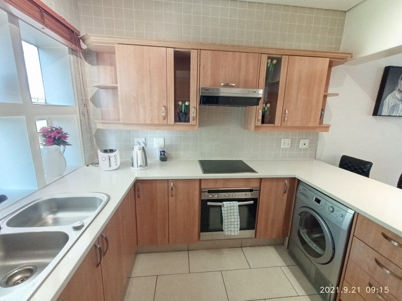 A functional kitchen featuring light wood-finish cabinetry, stone countertops, a built-in oven with hob, and a tiled backsplash.