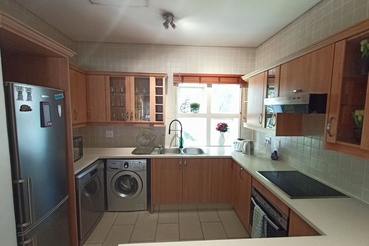 A functional kitchen featuring light wood cabinetry, stone countertops, tiled backsplash, and integrated appliances including an oven, hob, and laundry facilities.