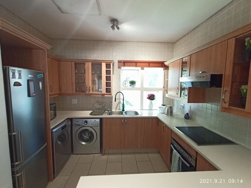 A functional kitchen featuring light wood cabinetry, stone countertops, tiled backsplash, and integrated appliances including an oven, hob, and laundry facilities.