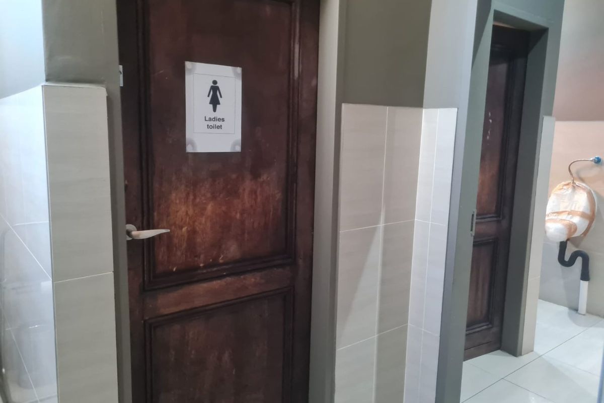 Commercial restroom area featuring tiled walls and flooring with wooden doors leading to individual stalls.