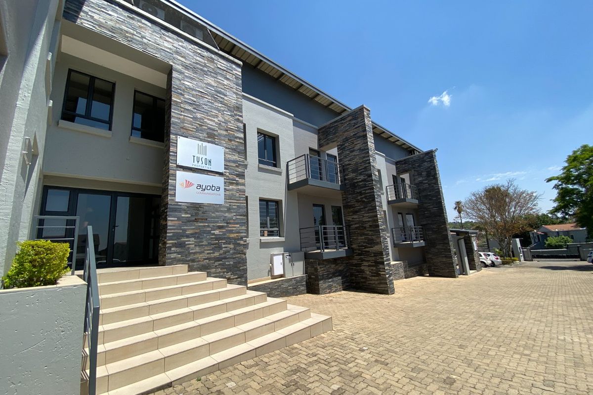 Modern commercial building exterior featuring stone cladding, paved driveway, and multiple balconies with metal railings.