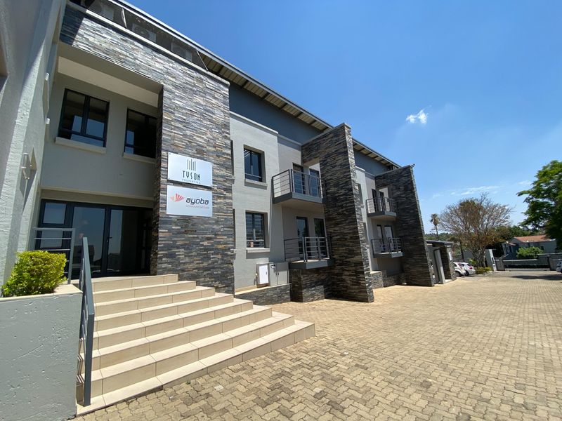 Modern commercial building exterior featuring stone cladding, paved driveway, and multiple balconies with metal railings.