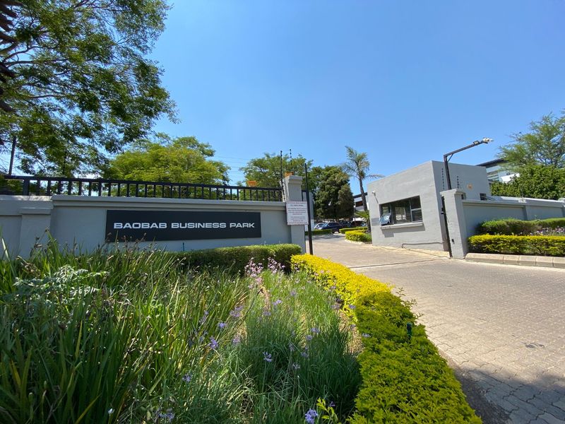 Entrance view of Baobab Business Park featuring a secure gatehouse, paved driveway, and perimeter wall with integrated electric fencing.