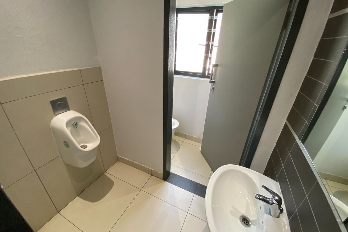 A clean commercial restroom facility featuring a wall-mounted urinal, a ceramic washbasin with chrome fixtures, and neutral tiled finishes.