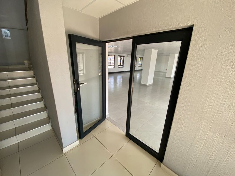 An open-plan commercial office space entrance featuring tiled flooring, glass doors, and a clean, neutral interior with structural columns and a suspended ceiling.