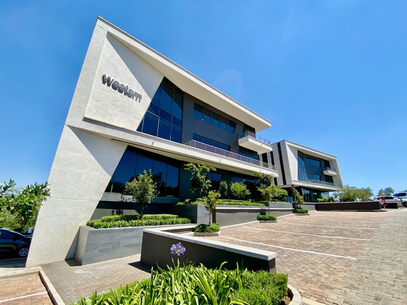 A modern commercial office building featuring a striking angular facade, glass curtain walls, and a well-maintained paved parking area with integrated landscaping.